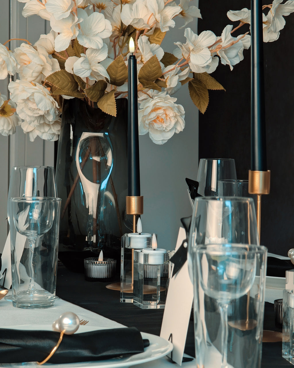 A black and white Decorative table setting with flowers, candles, and glasses on a dark surface.
