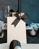 White name card with a black ribbon on a table setting with candles and glasses. For a black and white tablescape