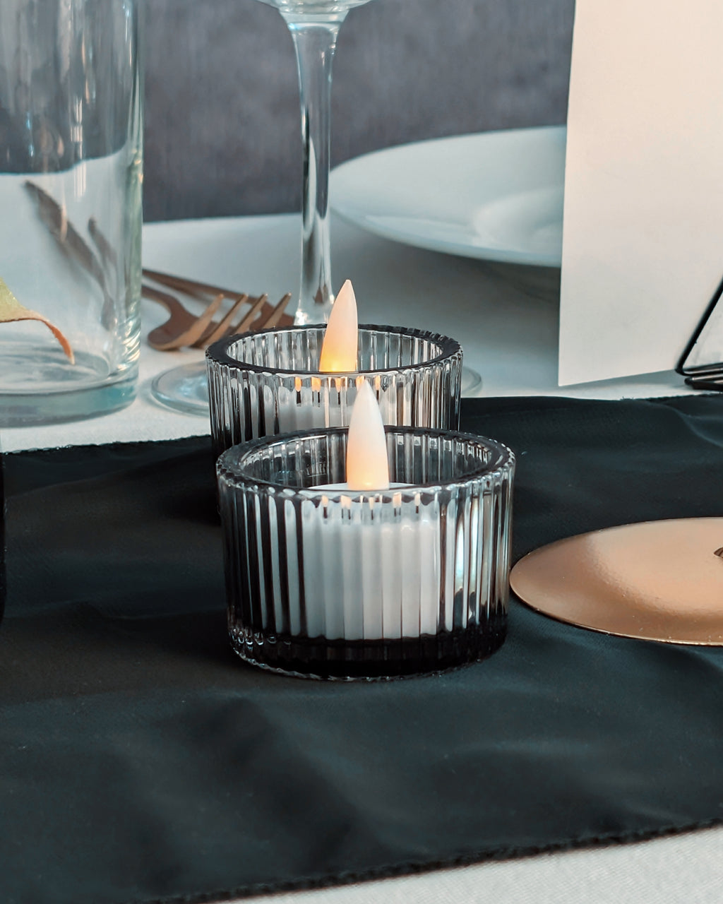 Two candle holders with lit candles on a table setting.