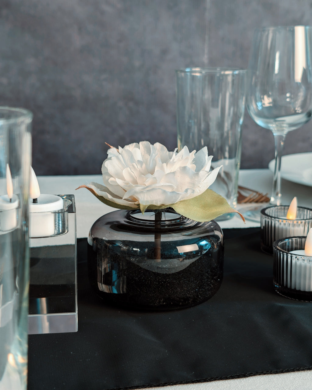 Decorative flower arrangement in a black vase on a table with candles and glasses.