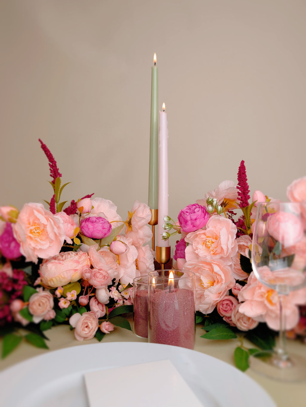 Table setting with pink flowers, candles, and glasses on a neutral background