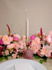 Table setting with pink flowers, candles, and glasses on a neutral background