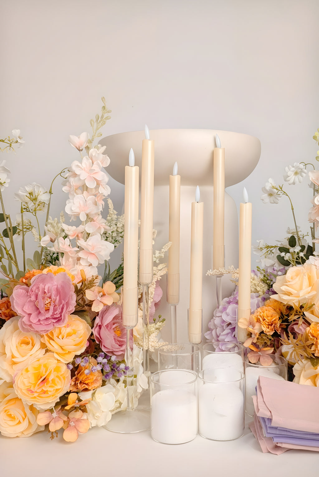 Candle holder with lit candles surrounded by flowers on a light background