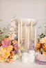 Candle holder with lit candles surrounded by flowers on a light background