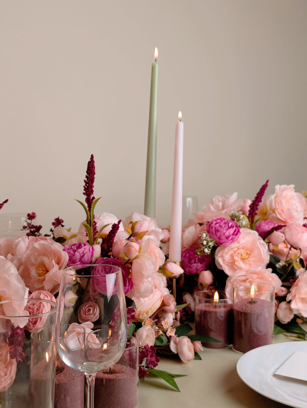 Table setting with pink flowers, candles, and glasses on a neutral background