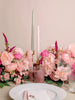 Table setting with pink flowers, candles, and glasses on a beige background