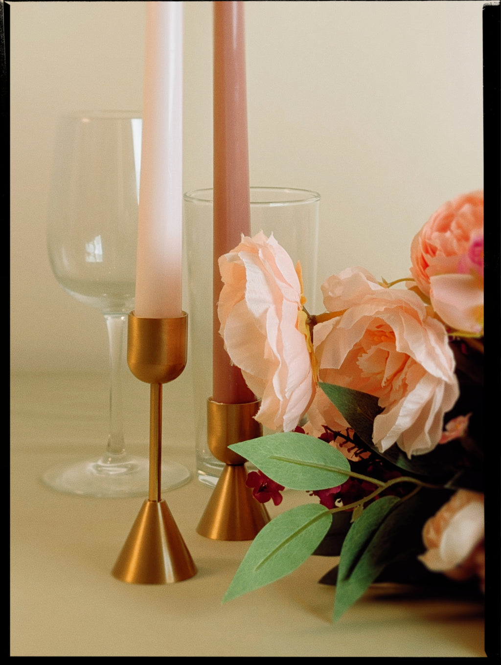 Decorative setup with candles, glasses, and flowers on a neutral background