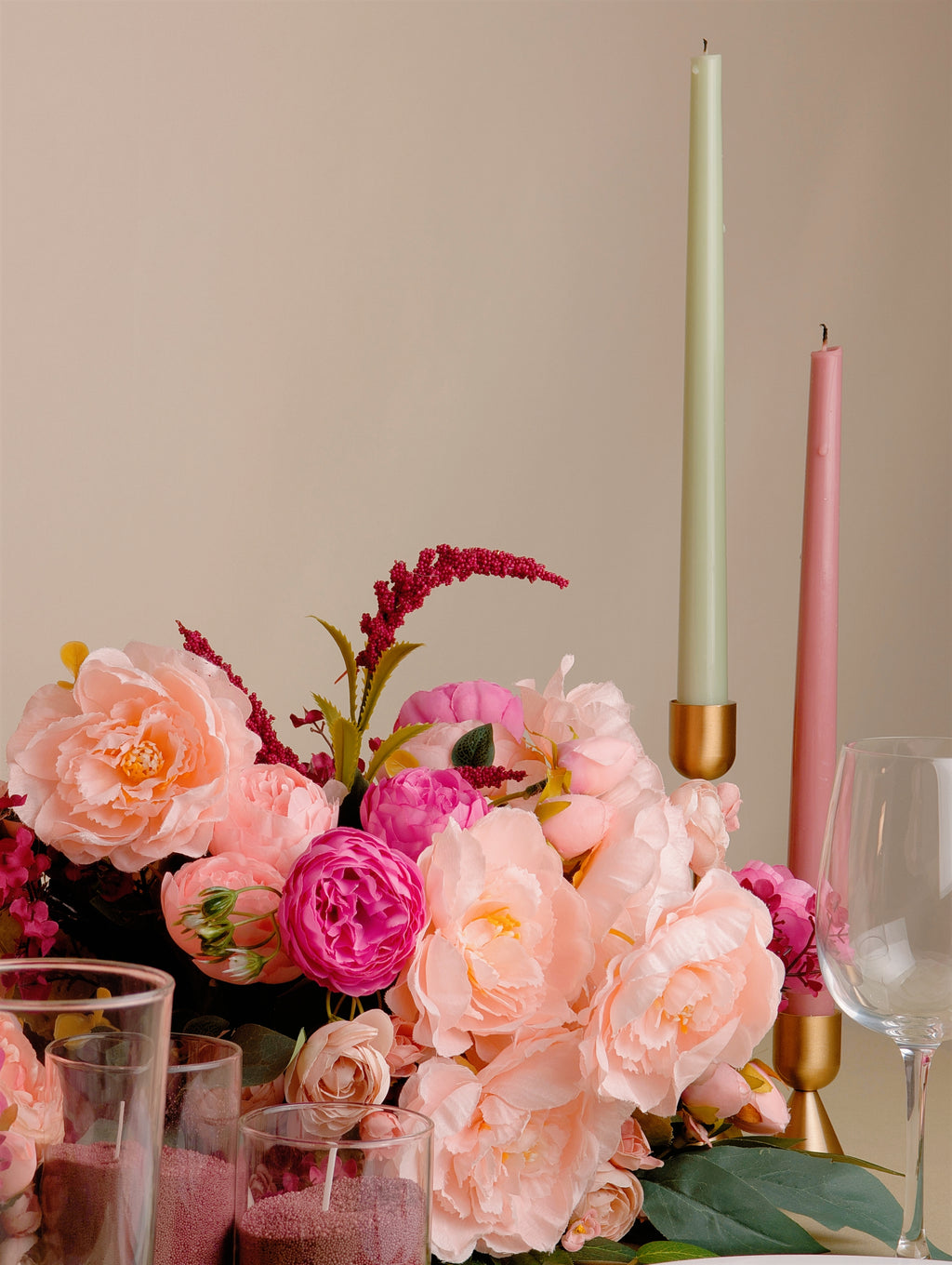 Table setting with pink and peach flowers, candles, and glasses on a neutral background