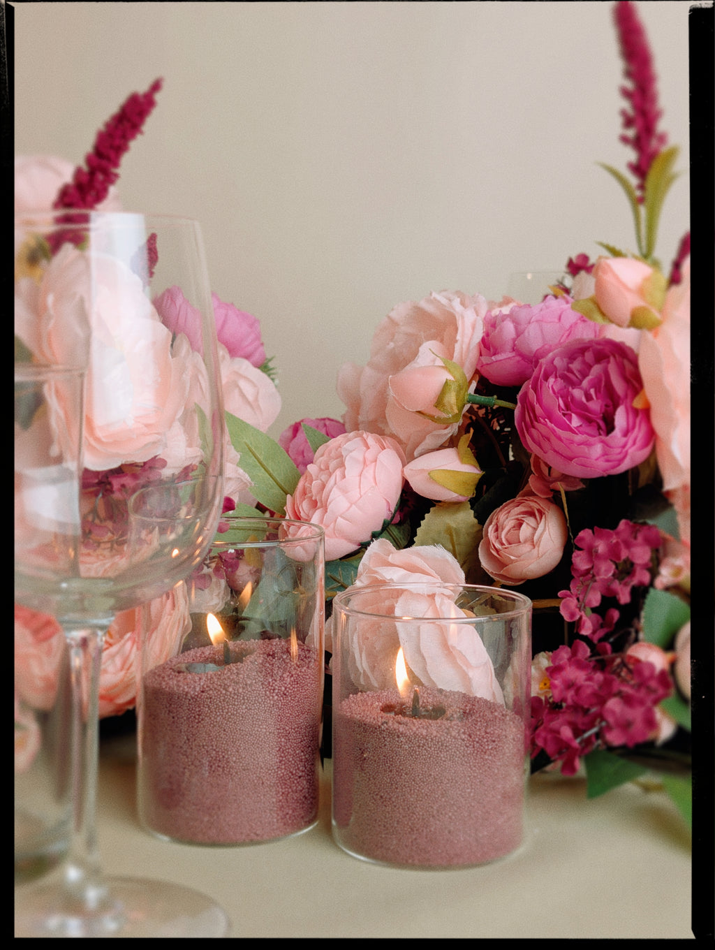 Decorative setup with pink sand candles and flowers on a table.