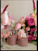 Decorative setup with pink sand candles and flowers on a table.